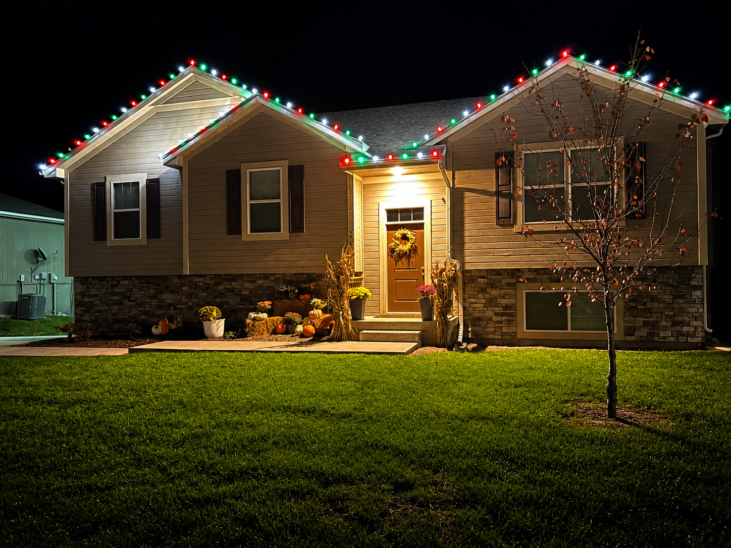 Split-level home with red, green, and white lights and fall porch decor