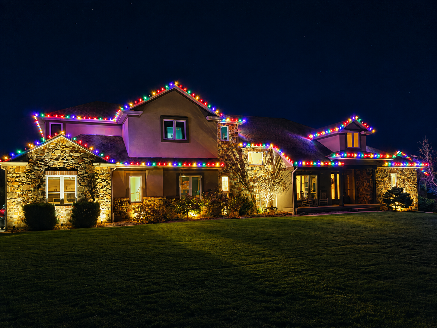 Large stone home outlined with multicolor Christmas lights installed by Parks on the Roof